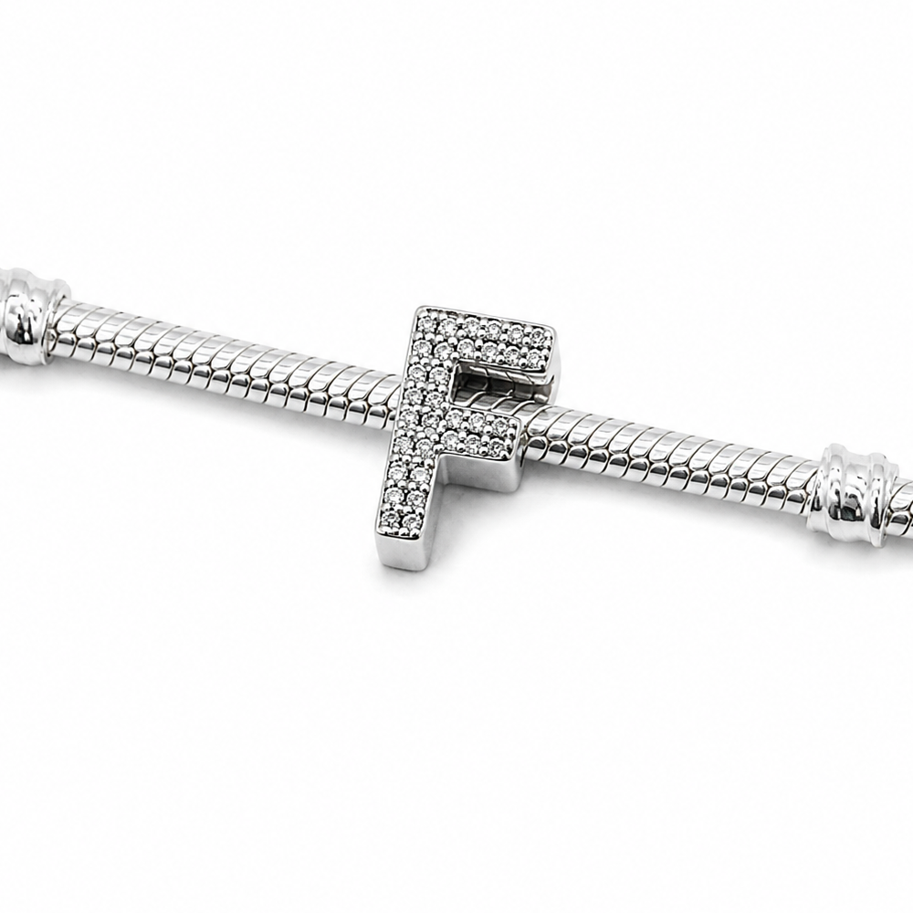 A silver-toned snake chain bracelet featuring a central sterling silver letter 'F' charm paved with small clear stones, shown against a plain white background.