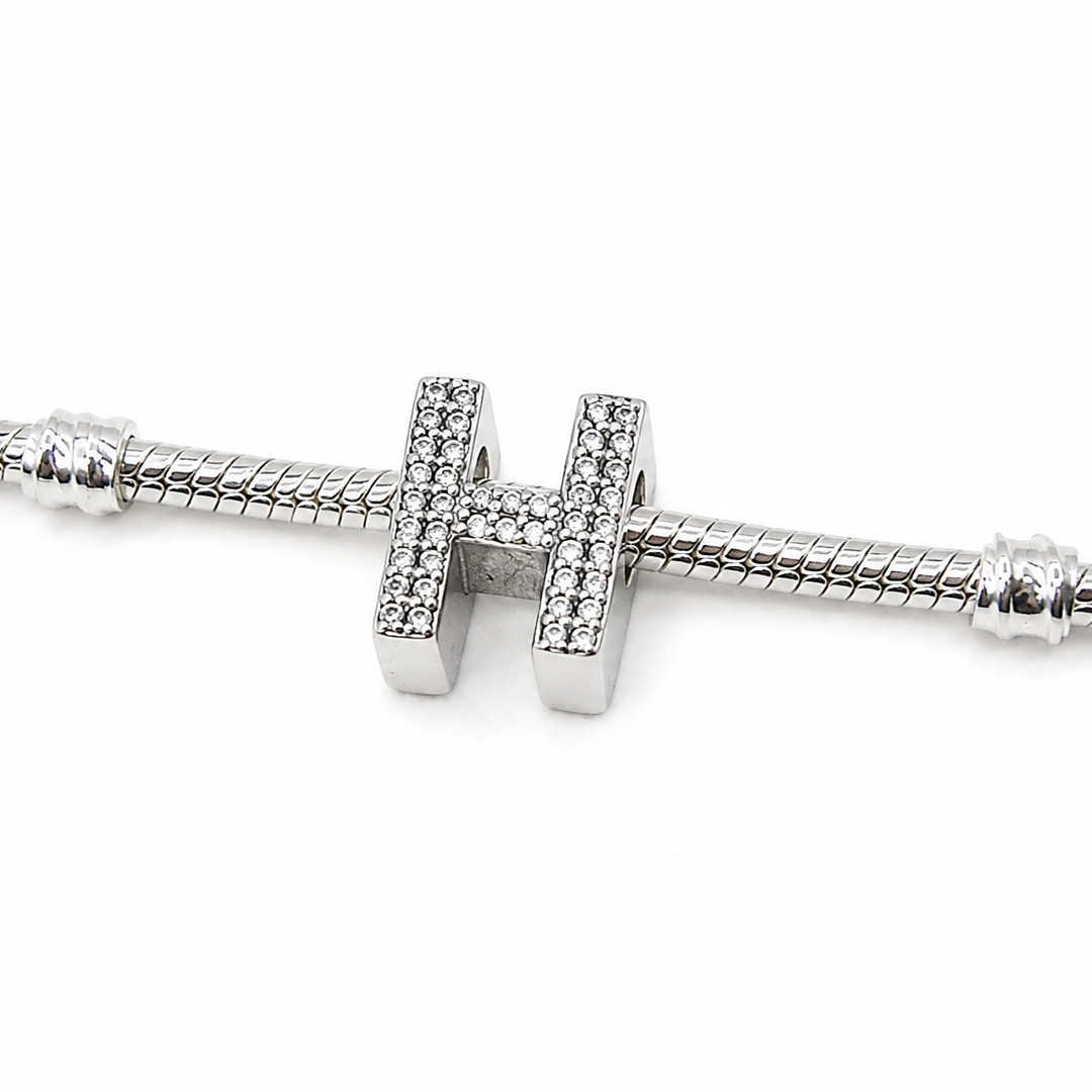 A sterling silver letter 'H' charm embellished with pavé-set clear crystals, threaded onto a silver snake chain bracelet against a white background.