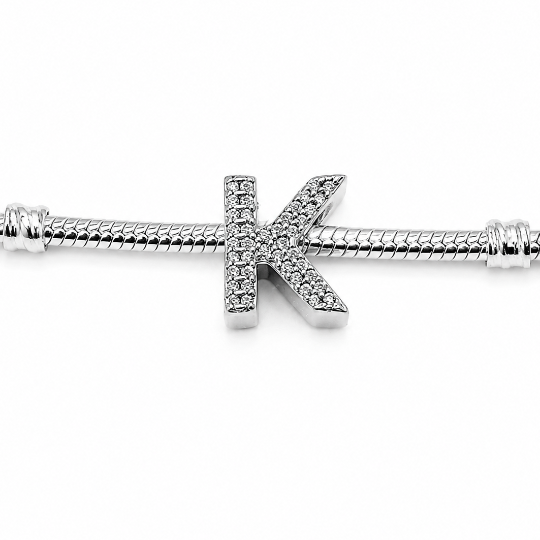 A silver-toned snake chain bracelet featuring a central letter 'K' charm paved with small clear stones, shown against a plain white background.