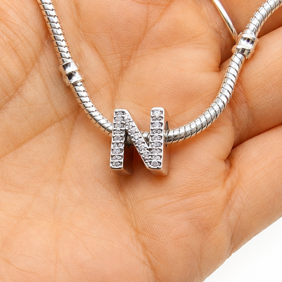 A silver snake chain necklace with a letter 'N' initial pendant encrusted with small clear stones, held in a person's open palm against a white background.