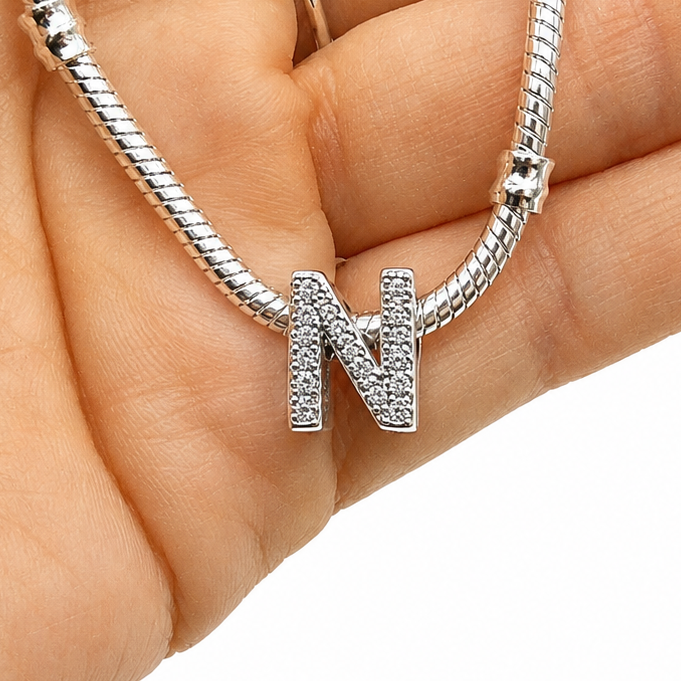 A silver snake chain necklace with a pavé-set letter 'N' pendant, held in a person's hand against a white background.