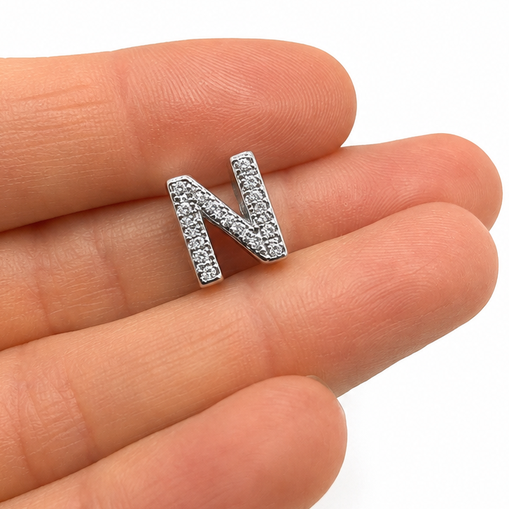 A sterling silver letter 'N' charm bead embellished with clear rhinestones, on fingertips for scale and shown on a plain white background.