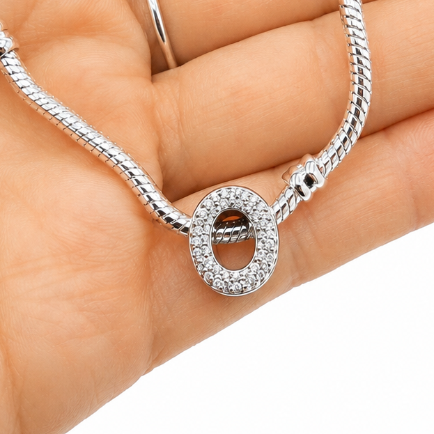 A silver-toned snake chain necklace with a sterling silver letter 'O' charm bead embellished with clear rhinestones, held in the palm of a hand against a white background.