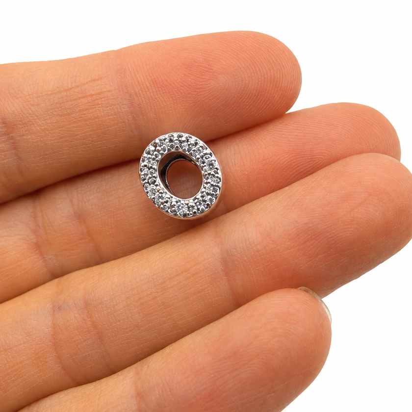 A sterling silver letter 'O' charm bead embellished with clear rhinestones, resting on the palm of a hand for scale against a white background.